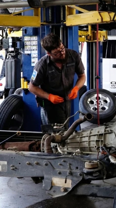 Woodlands Car Care technician working on a vehicle on a lift inside the collision shop in The Woodlands, TX