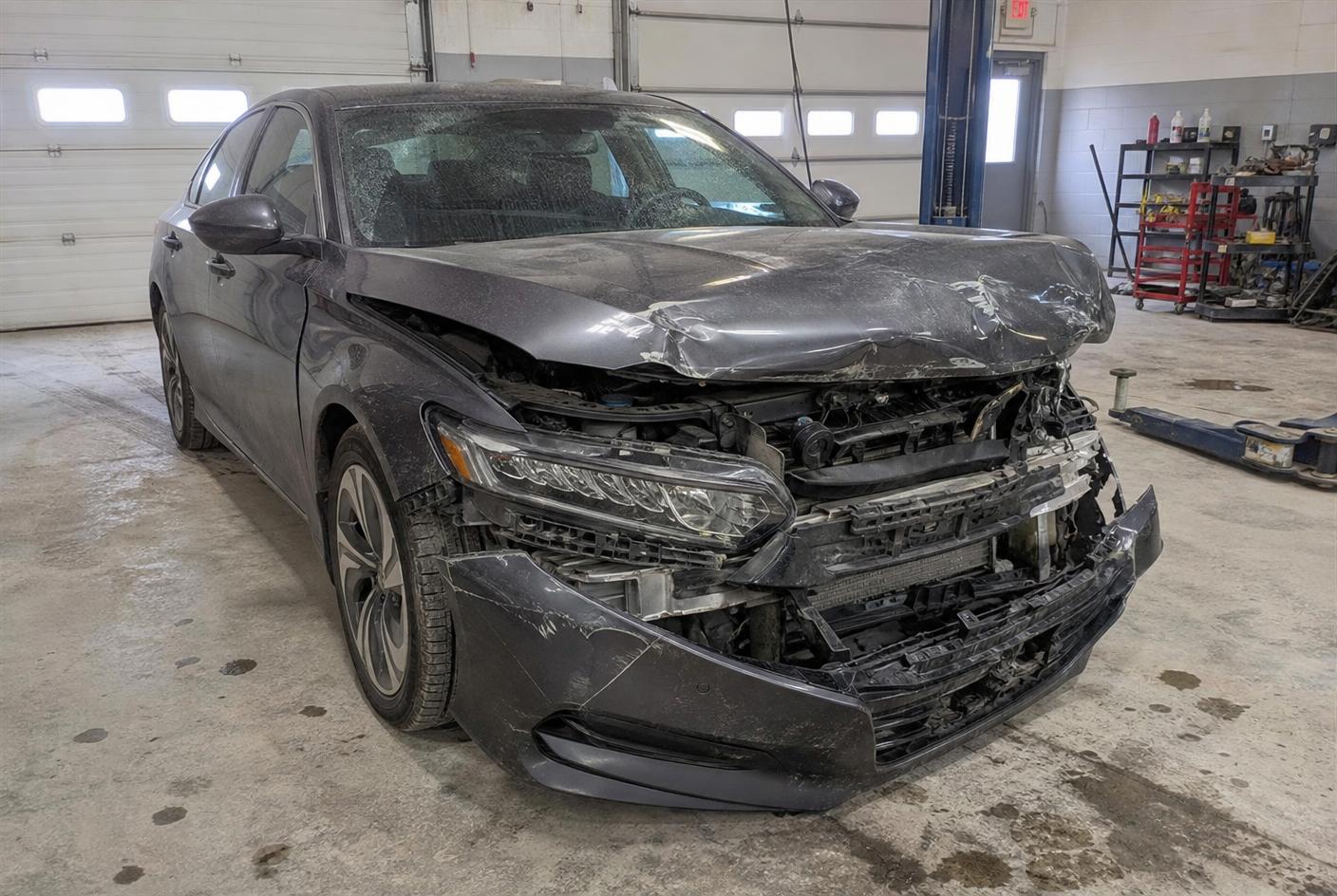 Gray sedan with a crushed front bumper, buckled hood and exposed radiator support before repair