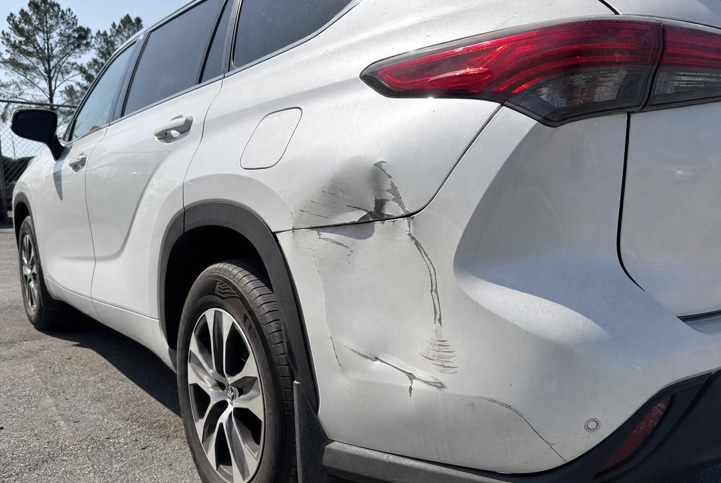 White SUV rear quarter panel with a deep crease dent and scraped paint before repair