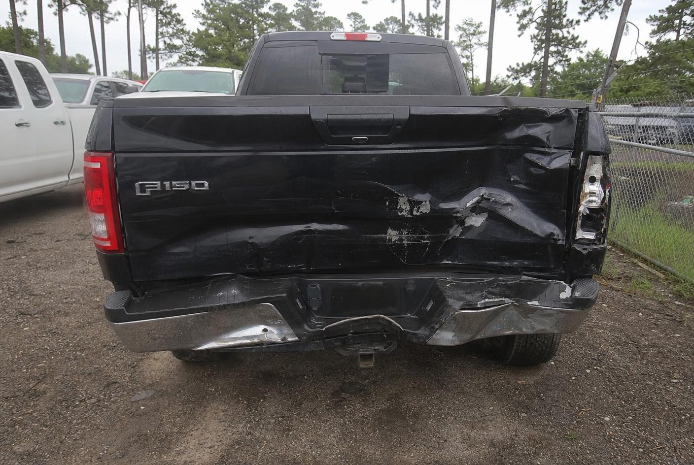 Black pickup truck with a crumpled tailgate and rear bumper damage before repair